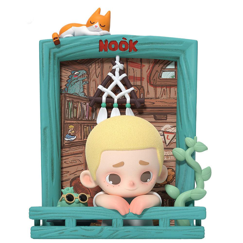 Toy figure with a teal frame and a character with blonde hair and sunglasses, set against a wooden interior background.