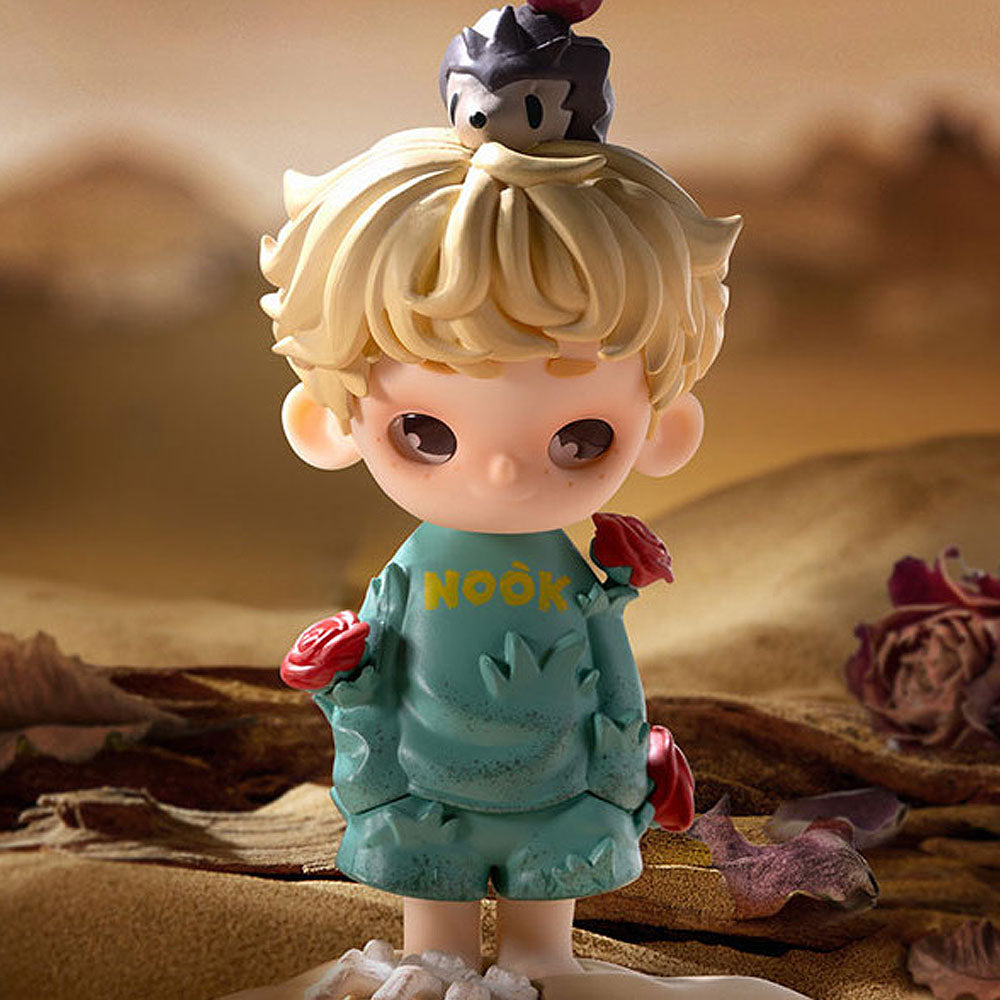 Toy figure of a character with blond hair and a blue shirt, standing in a desert-like setting.