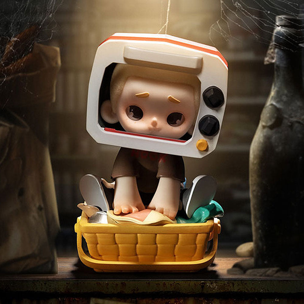Toy figure with a TV head sitting in a yellow basket in a dark, eerie setting.