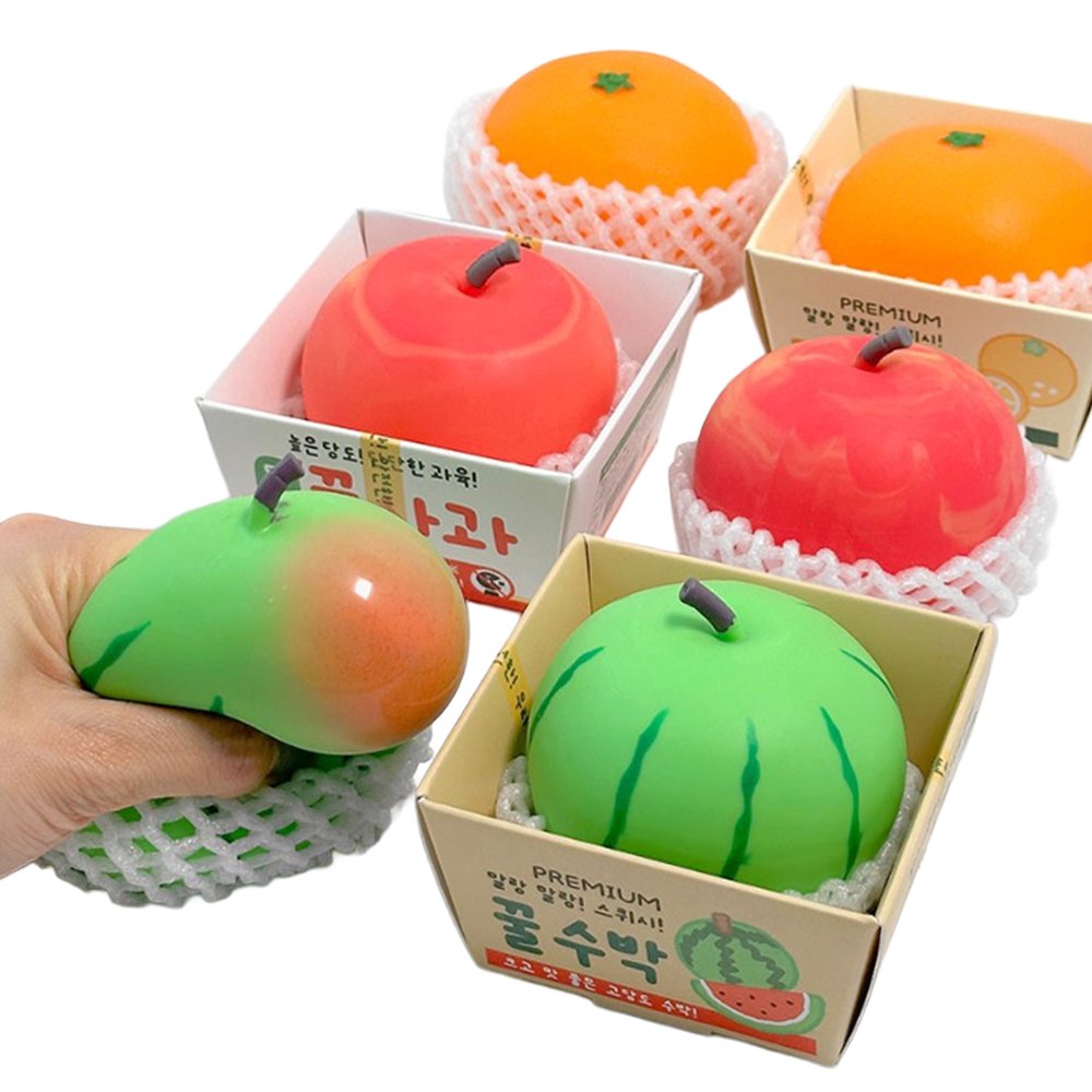 Vibrant fruit-shaped squishy stress toys styled like fresh apples, tangerines, and watermelons sitting in white foam protective netting and mini cardboard crates