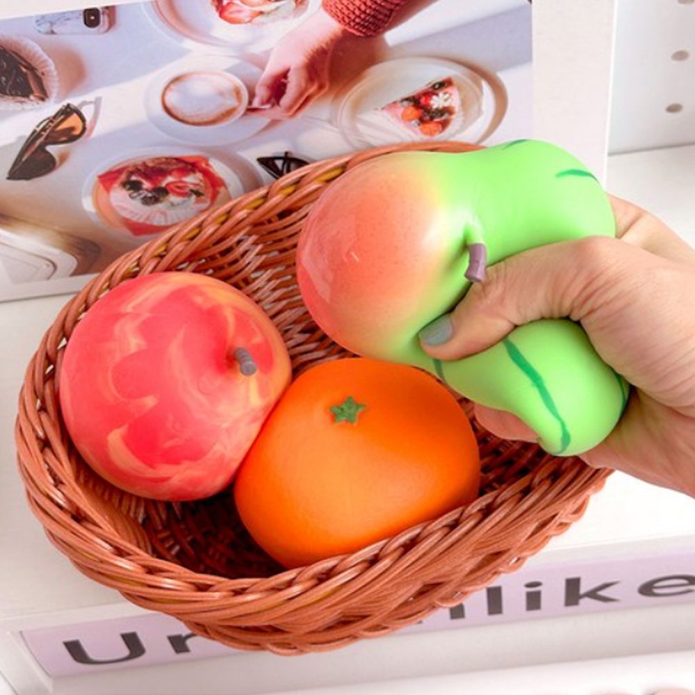 Vibrant fruit-shaped squishy stress toys styled like fresh apples, tangerines, and watermelons sitting in white foam protective netting and mini cardboard crates