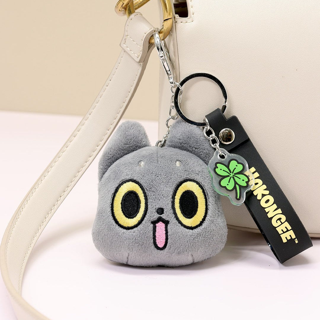 Black cat plush keychain with cute face on a white strap, attached to a white handbag.