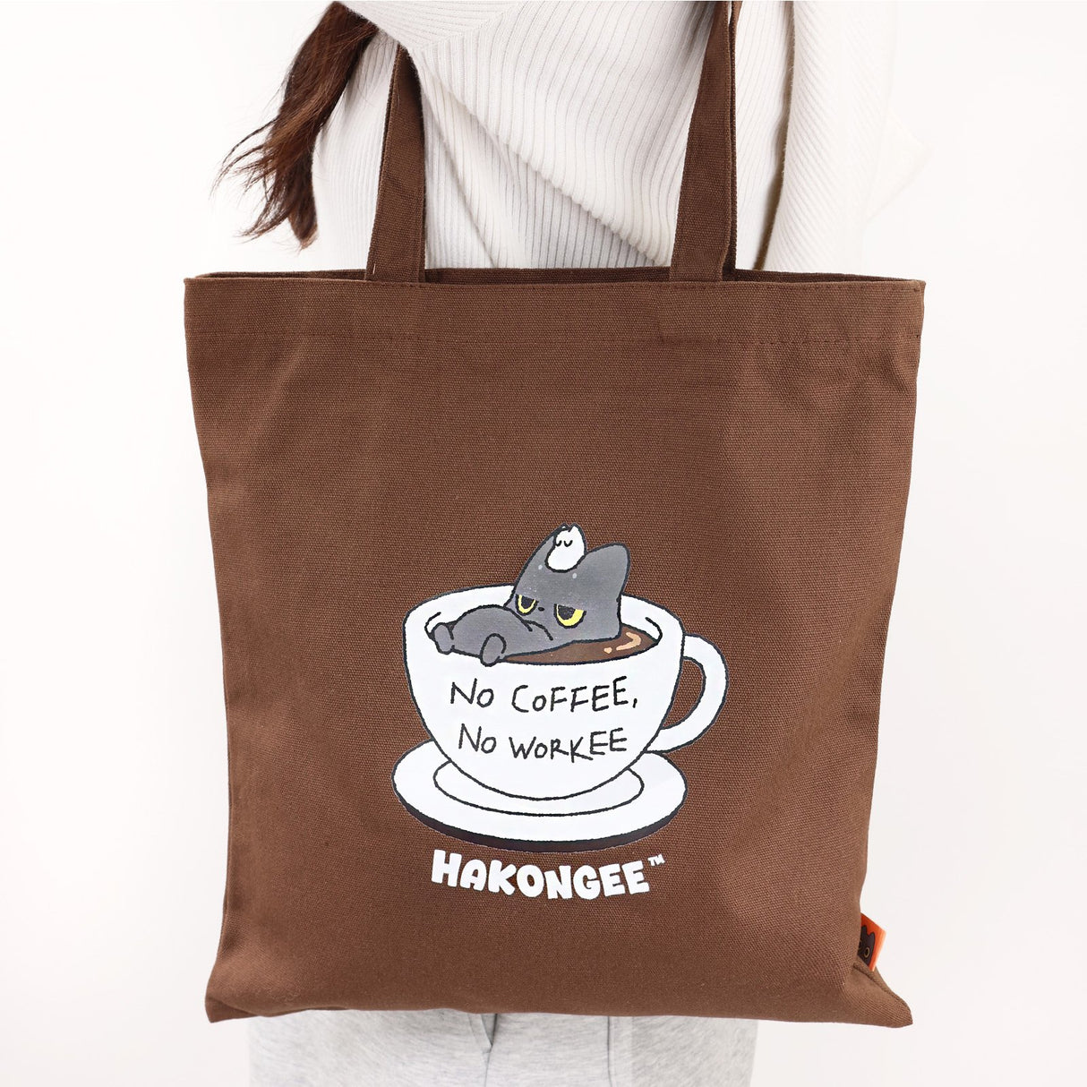 Brown tote bag with a black cat in a coffee cup design and 'Hakongee' branding.