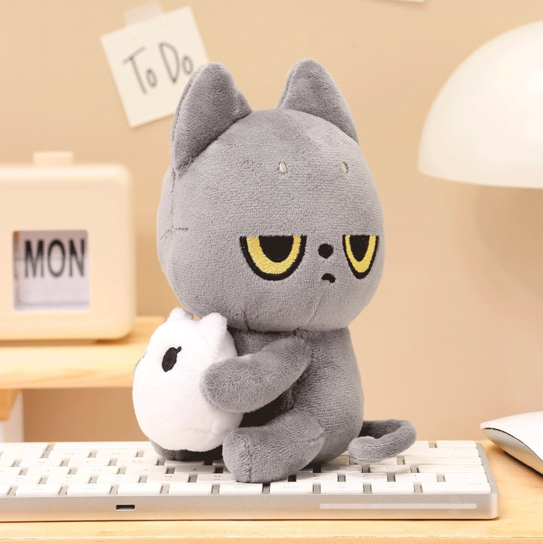 Black Cat plush cat toy holding a white Snoozy on a desk with a beige wall and 'To Do' notes in the background.