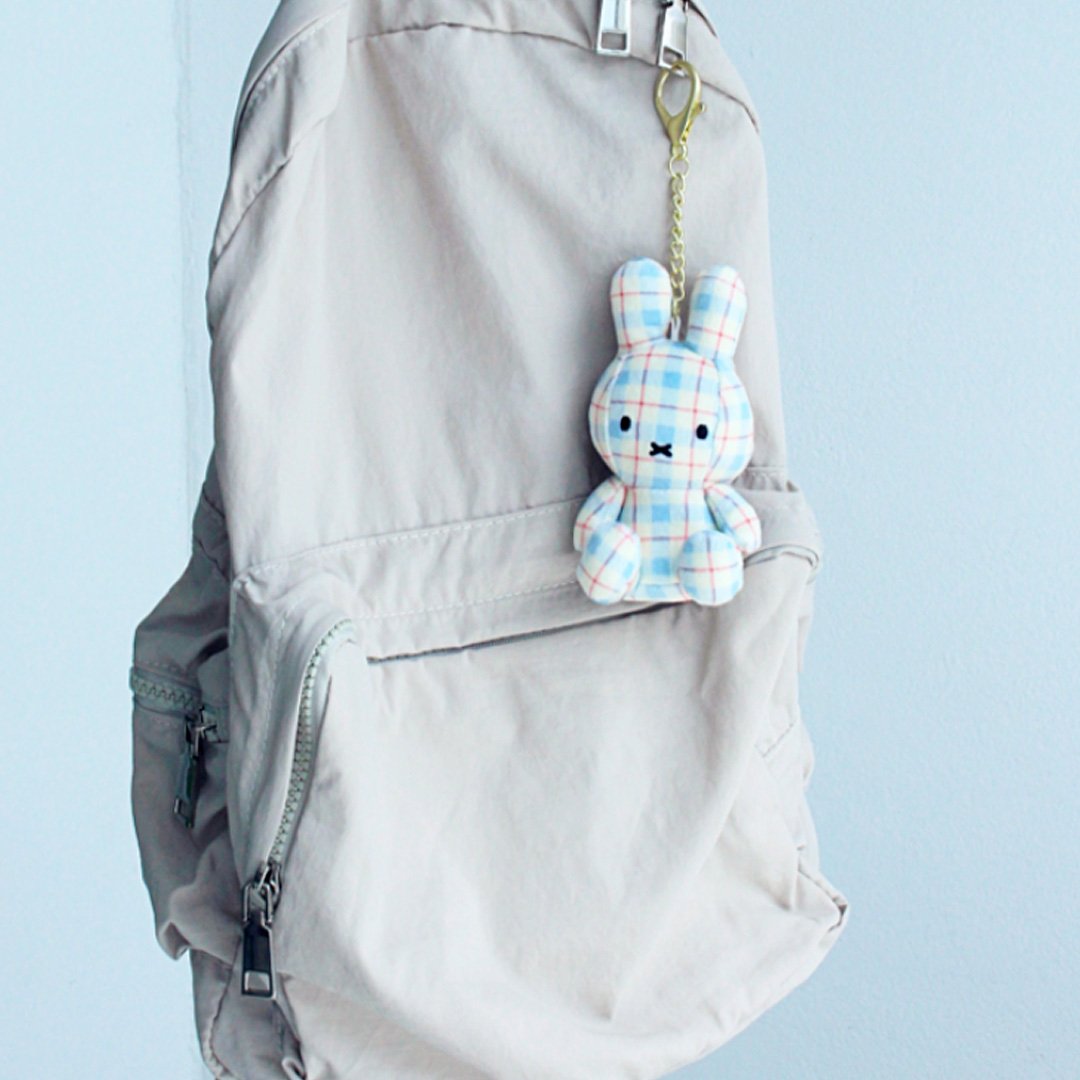 Officially licensed Miffy plush keychain featuring a blue and white plaid/checkered fabric pattern. he soft plush toy keychain attached to a gray backpack against a light blue background