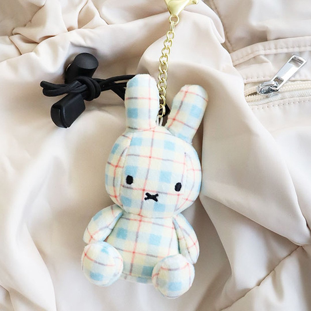 Officially licensed Miffy plush keychain featuring a blue and white plaid/checkered fabric pattern. The soft plush toy keychain attached to a beige backpack .