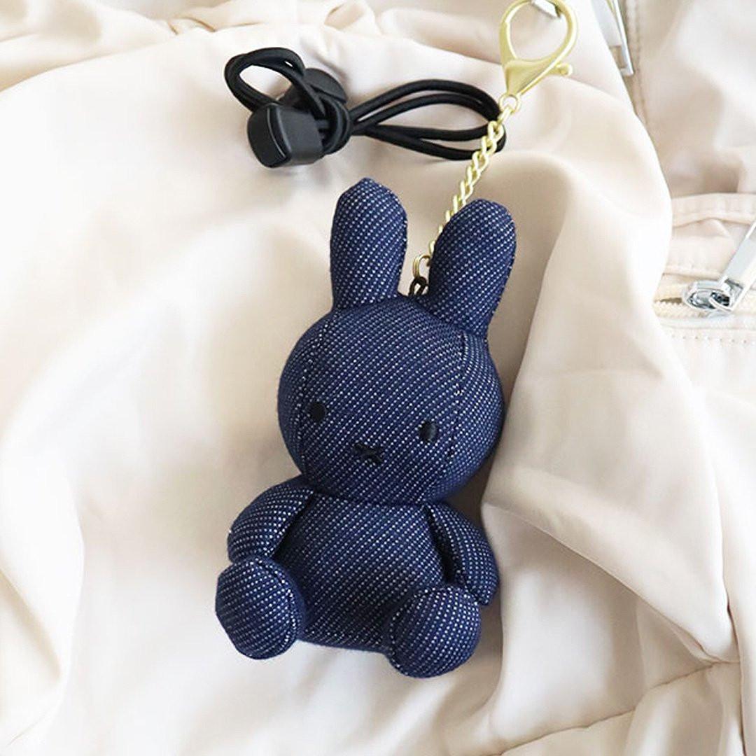 Officially licensed Miffy plush keychain featuring a denim fabric . The soft plush toy keychain attached to a beige backpack.