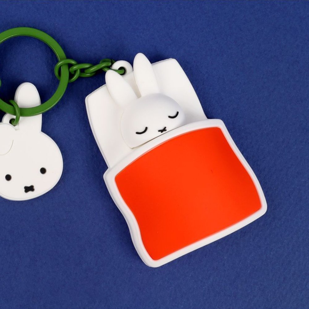 A collection of Miffy dream figure keychains in various poses, including Miffy reading a book, sleeping on a moon, and holding a yellow star, shown with green and blue accessories.