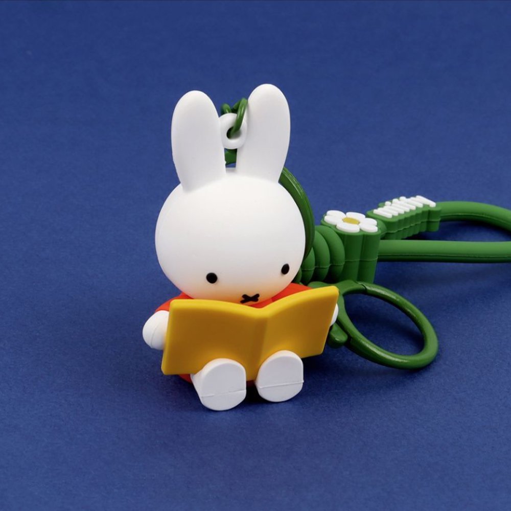 A collection of Miffy dream figure keychains in various poses, including Miffy reading a book, sleeping on a moon, and holding a yellow star, shown with green and blue accessories.