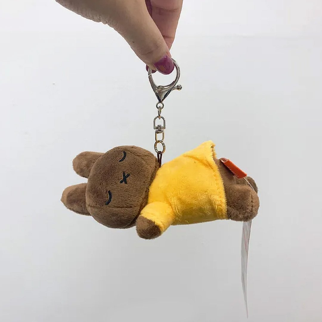 Officially licensed Melanie sleeping plush keychain featuring embroidered closed eyes and an 'X' mouth. Brown plush wearing yellow top. Ideal collectible bag charms, backpack zipper pulls or gift.