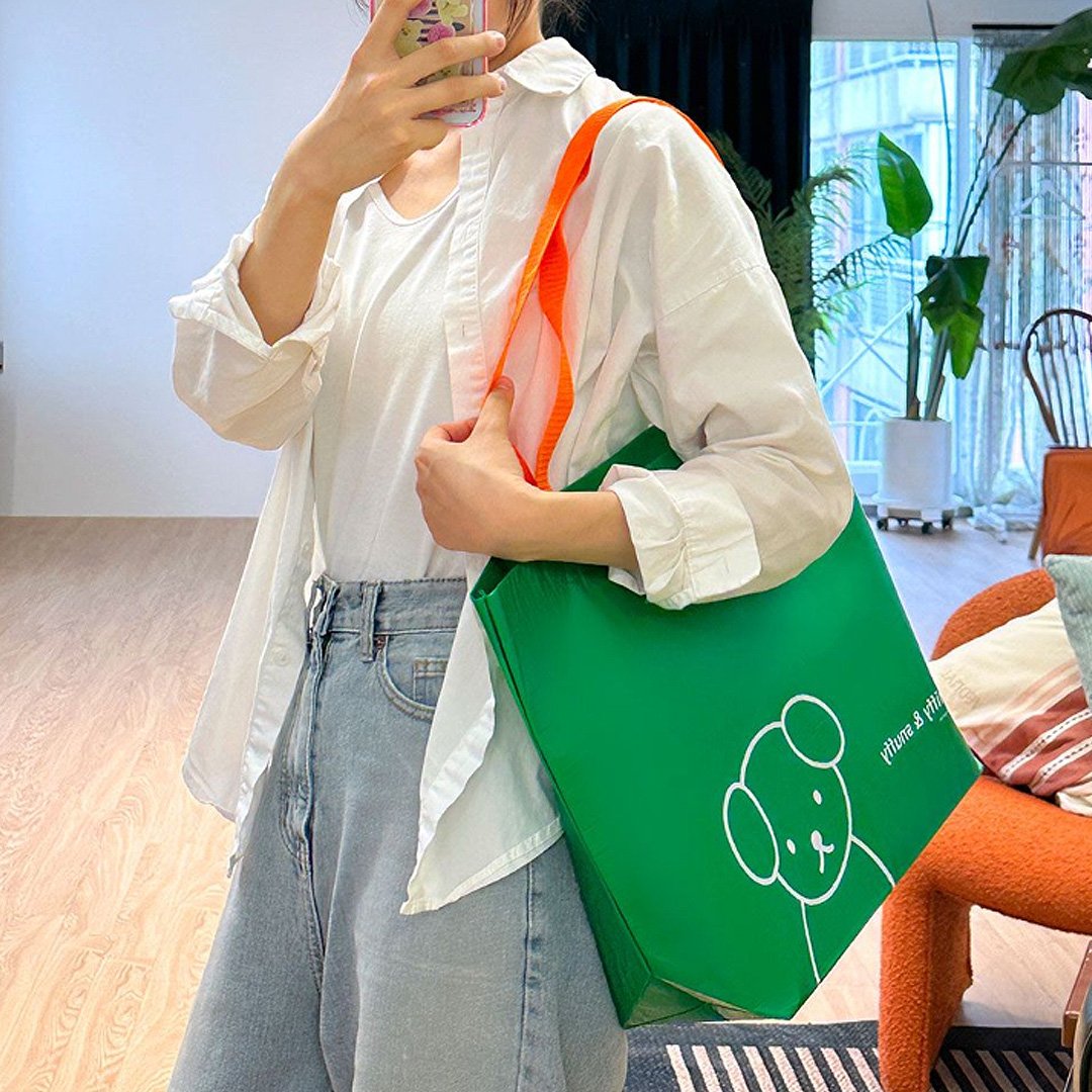 Person holding Officially licensed Miffy & Snuffy Reusable Shopping Bags. Made from durable, wipeable tarpaulin material. Bright Green bag with Snuffy and the "miffy & snuffy" text. Excellent for groceries and heavy-duty utility.