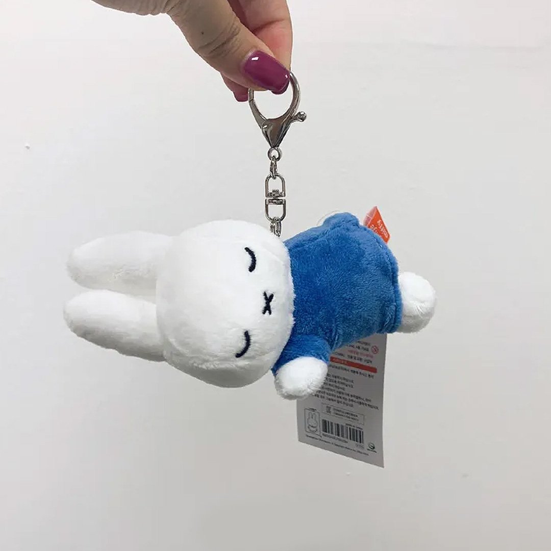 Officially licensed Miffy sleeping plush keychain featuring embroidered closed eyes and an 'X' mouth. Miffy plush wearing blue top. Ideal collectible bag charms, backpack zipper pulls or gift.