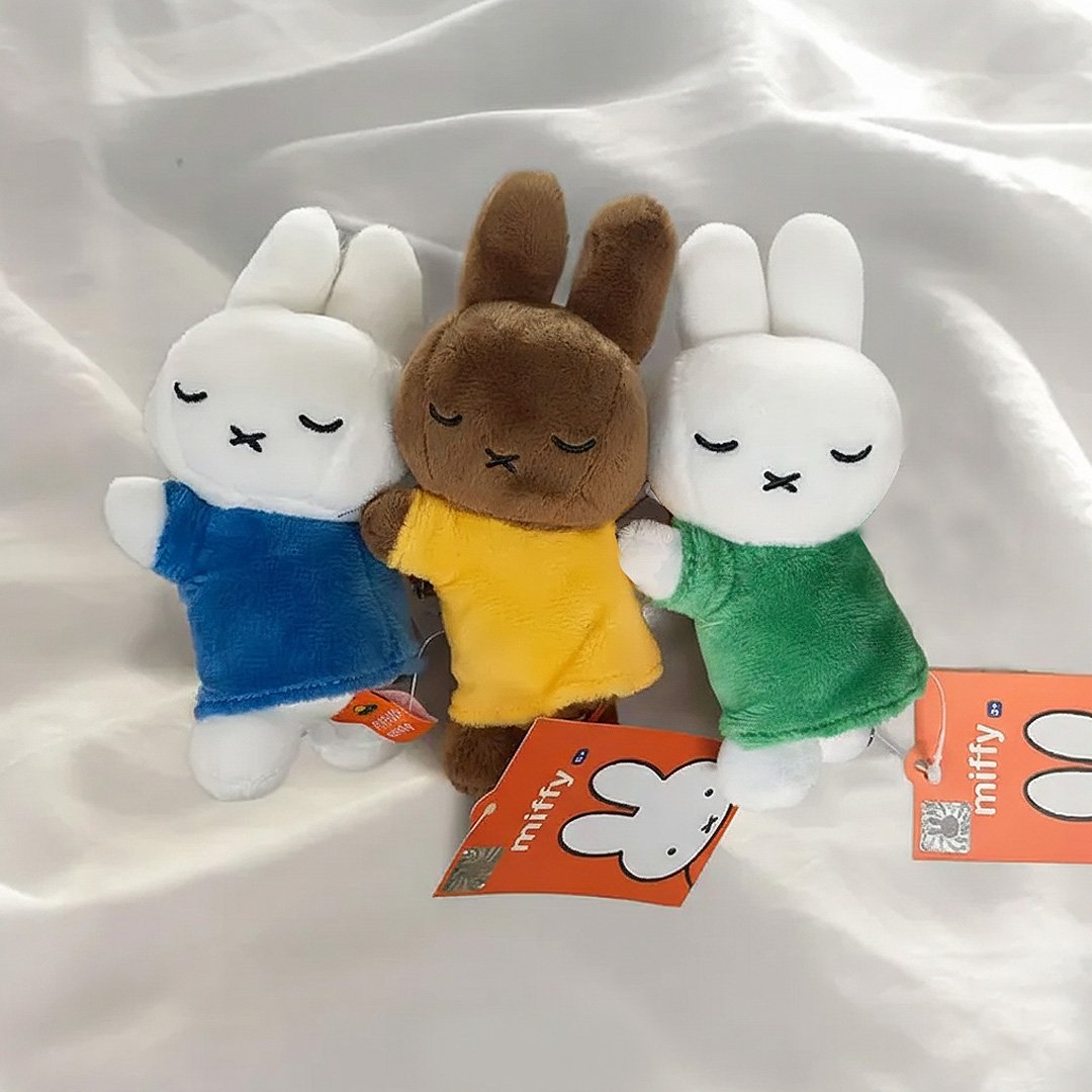 Set of three officially licensed Miffy plush sleeping keychains. The soft dolls include two white Miffy plush (wearing green and blue top ) and one brown Miffy plush(wearing a yellow top), all with embroidered closed eyes and an 'X' mouth. Ideal collectible bag charms or backpack zipper pulls.