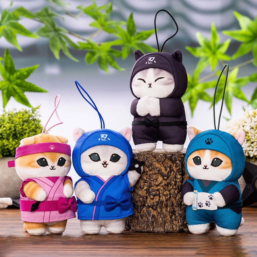 A collection of four officially licensed Mofusand ninja cat plush keychains featuring Pink Kunoichi, a Blue Shinobi, a Shadow Black Ninja, and a Teal Scroll-Guardian. Each plush features intricate costume details, including headbands with paw-print emblems, fabric belts, and tiny ninja accessories like throwing stars or scrolls.