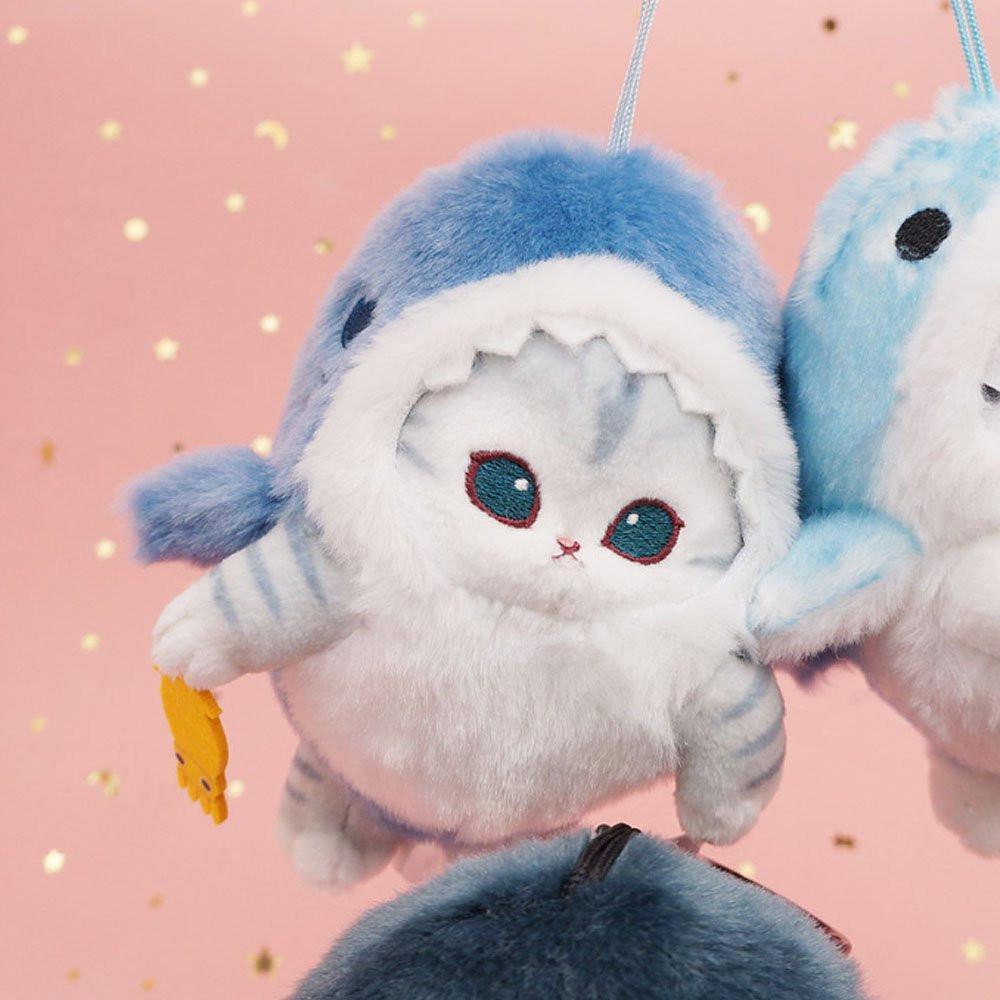 An officially licensed Mofusand shark cat plush keychain featuring a fluffy gray tabby kitten wearing a blue shark onesie with embroidered details