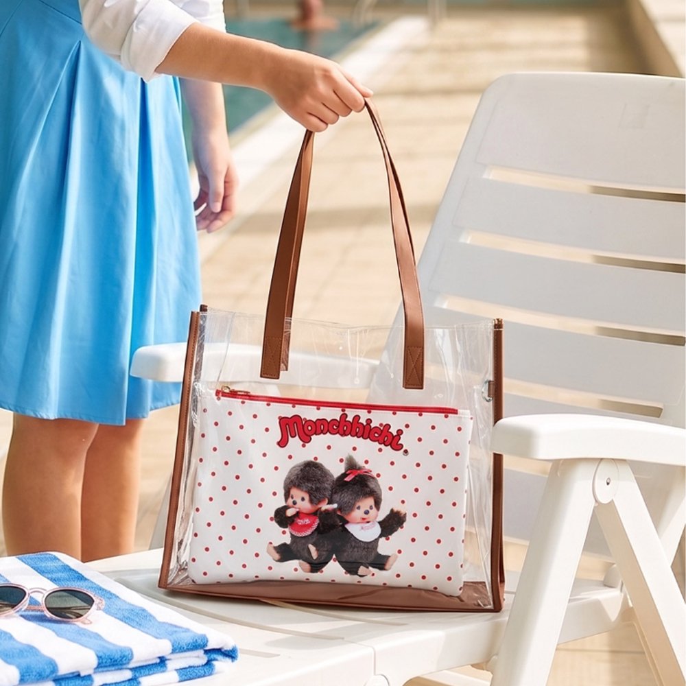 An officially licensed Monchhichi clear tote bag with a removable red polka-dot zippered inner pouch and long shoulder straps, available in black and brown trim
