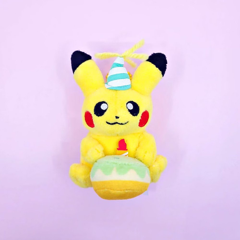 A Pokémon Pikachu plush keychain holding a celebration cupcake and wearing a striped party hat with yellow yarn on top, attached to a colorful ball chain