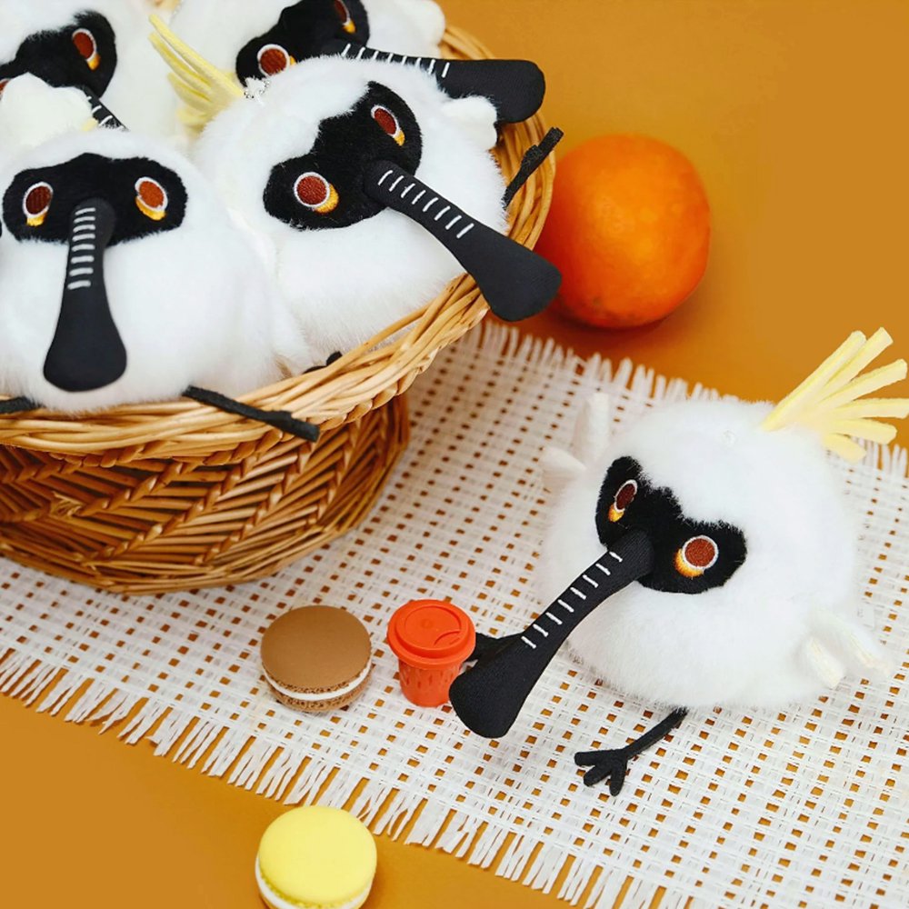 A round, fluffy Black-faced Spoonbill bird plush keychain with a distinctive long beak, a playful tuft of yellow fur, and small black feet