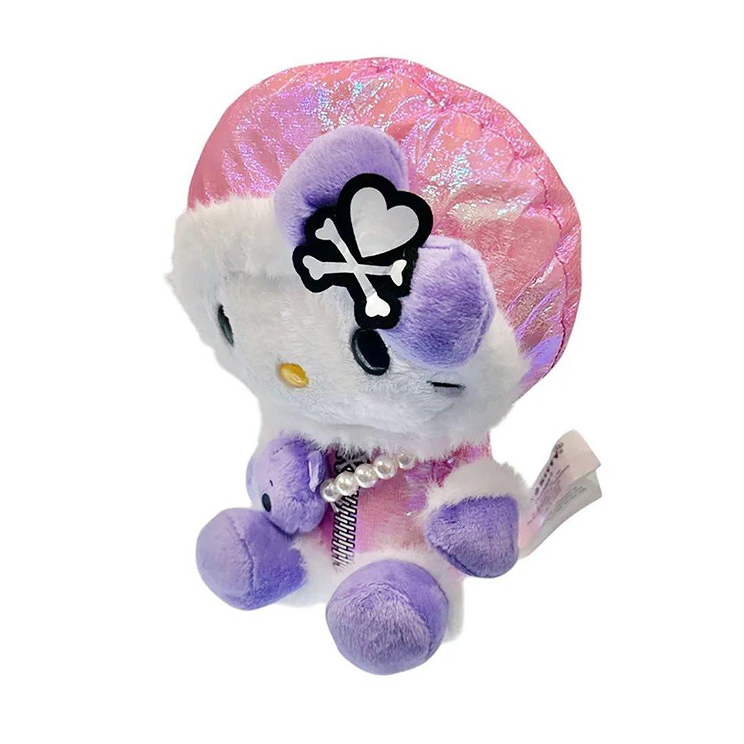 Hello Kitty x Tokidoki design is perfect for the holiday season. Hello Kitty sports a trendy look with an iridescent pink holographic beanie adorned with her signature purple bow decorated with a white heart and crossbones skull Tokidoki mark. She's dressed in a stylish pink holographic vinyl puffer jacket and holds an adorable purple bear plush with a pearl chain strap, giving her a fashionable streetwear vibe. Her soft plush body in white and purple creates the perfect bean doll silhouette for displaying