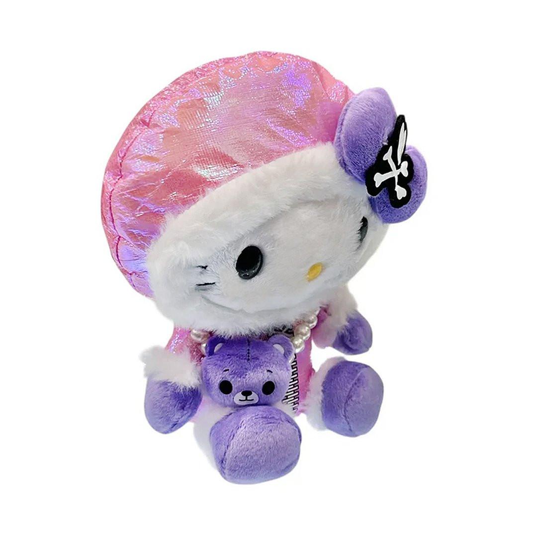 Hello Kitty x Tokidoki design is perfect for the holiday season. Hello Kitty sports a trendy look with an iridescent pink holographic beanie adorned with her signature purple bow decorated with a white heart and crossbones skull Tokidoki mark. She's dressed in a stylish pink holographic vinyl puffer jacket and holds an adorable purple bear plush with a pearl chain strap, giving her a fashionable streetwear vibe. Her soft plush body in white and purple creates the perfect bean doll silhouette for displaying