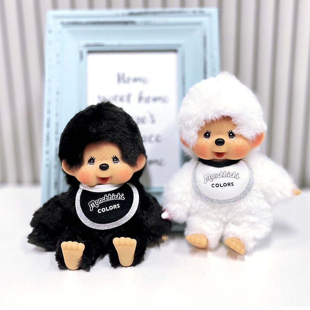 Two plush toys, one black and one white, with 'Monchhichi' branding on a light background.