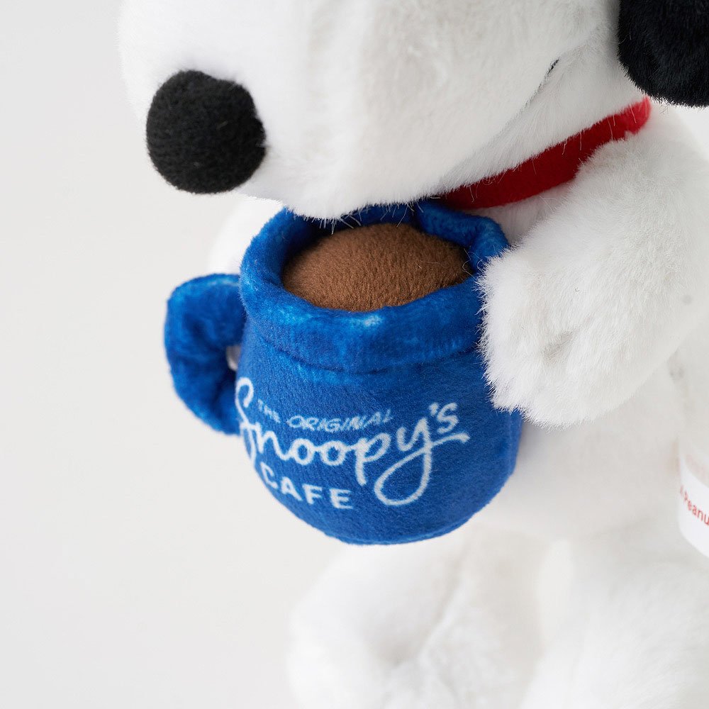 Plush Snoopy holding a blue mug with 'The Original Snoopy's Cafe' text on a white background