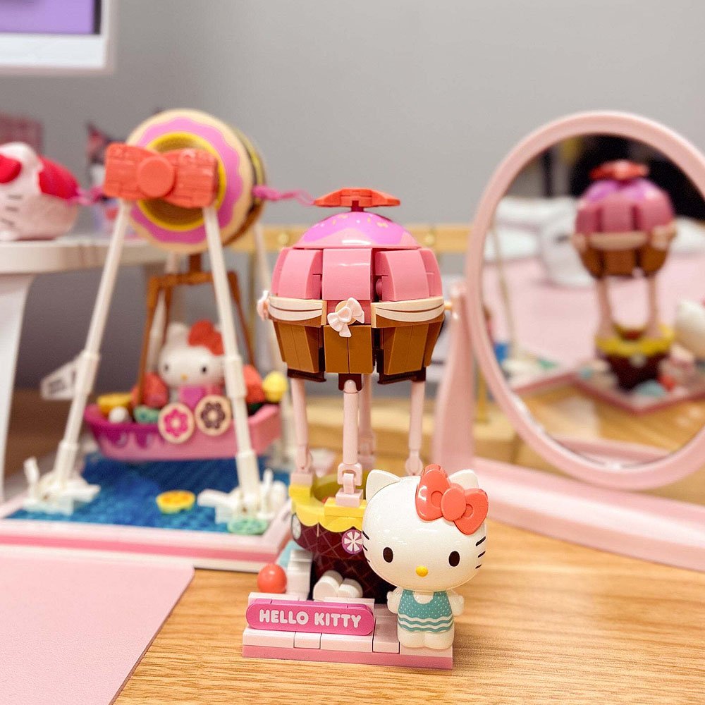 Hello Kitty toy figure with a pink and brown structure on a wooden surface.