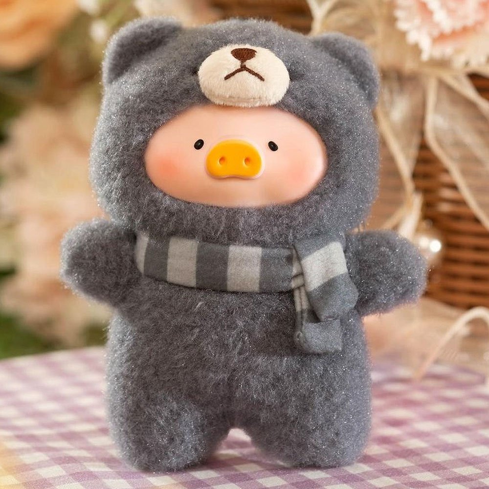 Plush toy bear in a gray outfit with a striped scarf on a checkered tablecloth.