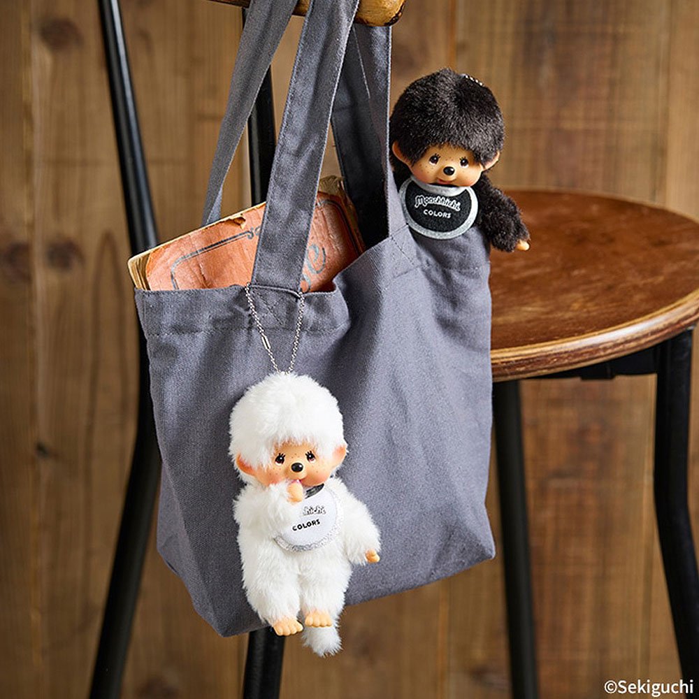 Gray tote bag with plush monkey dolls hanging from it on a wooden stool.