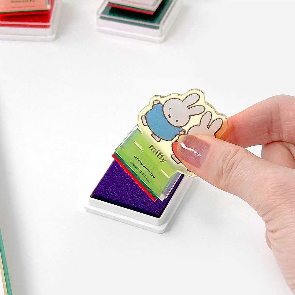 Hand holding a colorful rubber stamp with a Miffy character design on a white background.