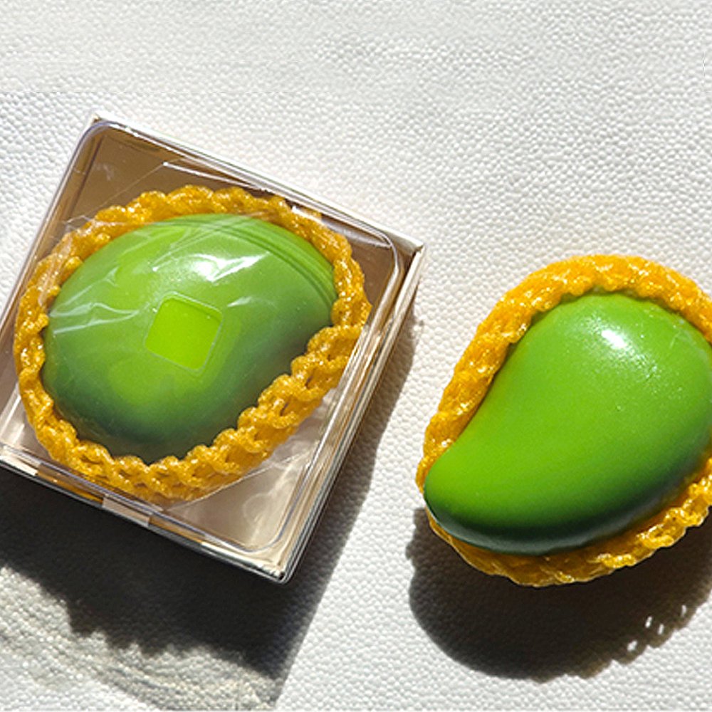 Sugar Mango Crunch Slime packaged in a clear square gift box with yellow fruit protective net mesh, looking like a real green mango, ideal holiday stocking stuffer and fun fidget present