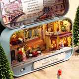 A intricate DIY miniature kit replicating a traditional Parisian cafe with a European designed facade, outdoor seating, and warm LED light