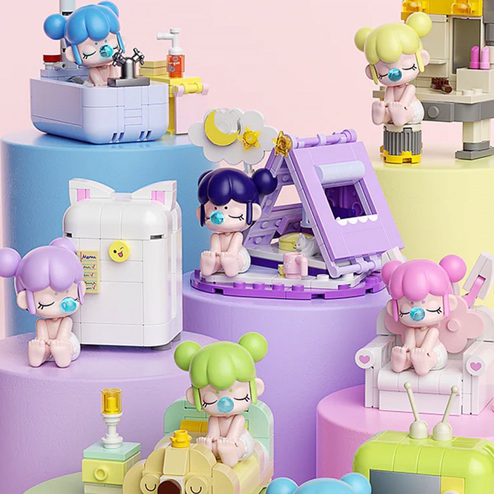 A collection of officially licensed building block sets featuring Baby Nanci in various home scenes like a bathtub, a bed, and next to a retro TV. The figures have colorful hair and are surrounded by pastel-colored furniture and accessories.