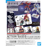 Two officially licensed Bandai Action Base 6 stands in clear plastic. Each features a rectangular base and an articulated support arm, customized with different plastic stickers showing portraits of characters like Suletta, Miorine, Guel, Shaddiq, and Elan.