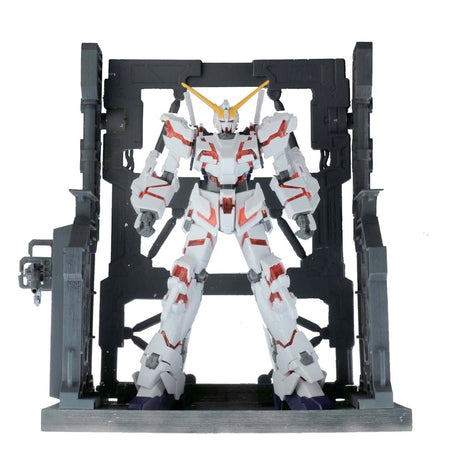 An officially licensed Bandai System Base 001 model kit display stand in metallic gunmetal gray. The retail packaging shows the mechanical hangar holding 1/144 scale Gunpla figures, highlighting its adjustable structural parts and industrial detail.
