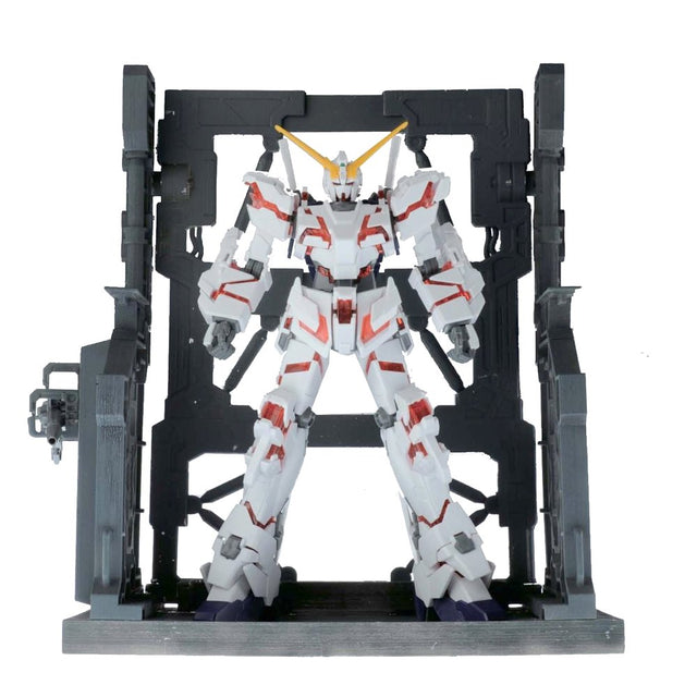 An officially licensed Bandai System Base 001 model kit display stand in metallic gunmetal gray. The retail packaging shows the mechanical hangar holding 1/144 scale Gunpla figures, highlighting its adjustable structural parts and industrial detail.
