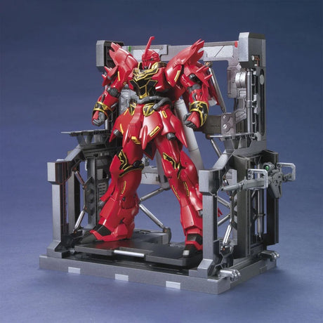 An officially licensed Bandai System Base 001 model kit display stand in metallic gunmetal gray. The retail packaging shows the mechanical hangar holding 1/144 scale Gunpla figures, highlighting its adjustable structural parts and industrial detail.
