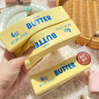 Realistic yellow butter stick squishy stress toy with blue lettering "4oz Salted Butter"