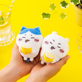 Two cute Chiikawa and Hachiware held in a hand against a yellow background with a glass of water and plant.