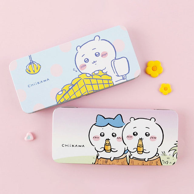 Two rectangular tin pencil cases featuring officially licensed Chiikawa artwork. One is light blue with white polka dots showing Chiikawa and a yellow claw machine hand. The other one has a pink-to-purple sunset gradient showing Chiikawa and Hachiware sitting on stumps and drinking.