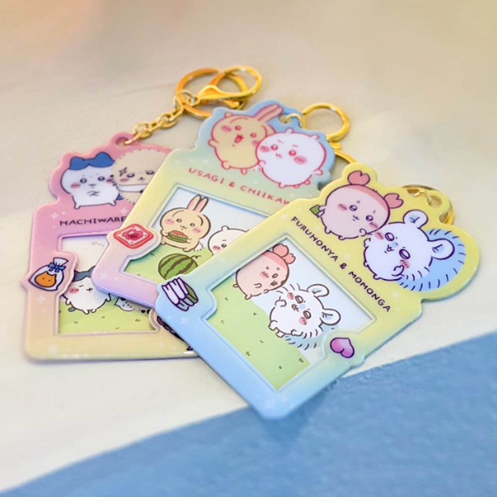 Colorful, officially licensed Chiikawa photo frame keychains featuring pastel gradients, character illustrations, and transparent window slots. Gold keyrings and lobster clasps are attached at the top of each charm holder.
