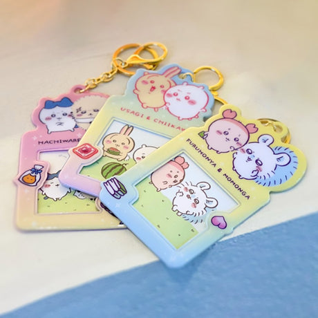 Colorful, officially licensed Chiikawa photo frame keychains featuring pastel gradients, character illustrations, and transparent window slots. Gold keyrings and lobster clasps are attached at the top of each charm holder.