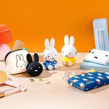 A curated collection of official Miffy rabbit merchandise displayed on a wooden desk, including white and blue figure night lights, silicon pouches, and a patterned pouch; minimalist desk decor and aesthetic daily organization accessories for an adult mental wellness workspace.