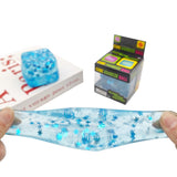 Translucent cube-shaped glitter squishy stress balls in purple, green, light blue, and pink filled with shimmering sparkles