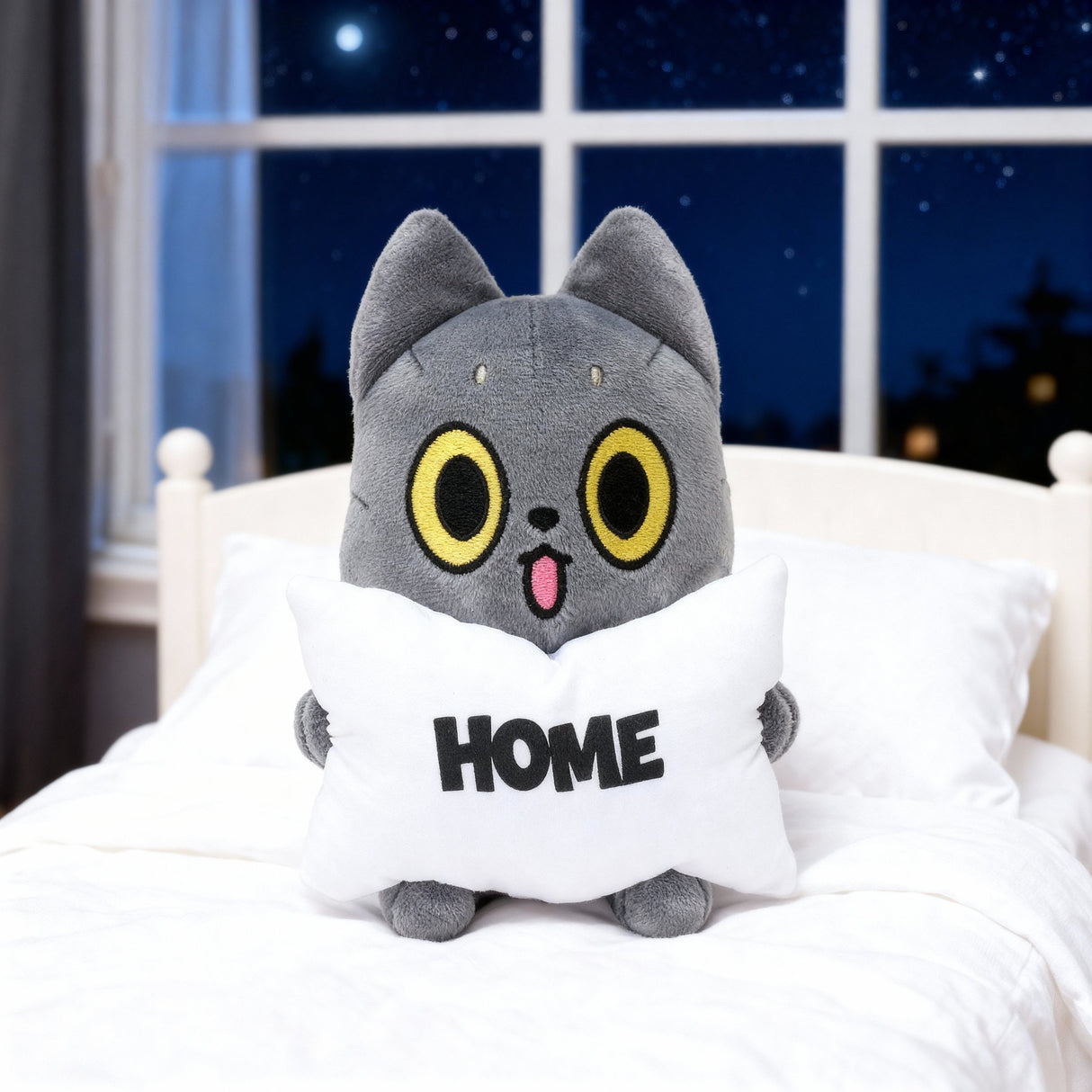 Hakogee black Cat plush toy with yellow eyes and a pink mouth on a pillow labeled 'HOME' in a bedroom setting.