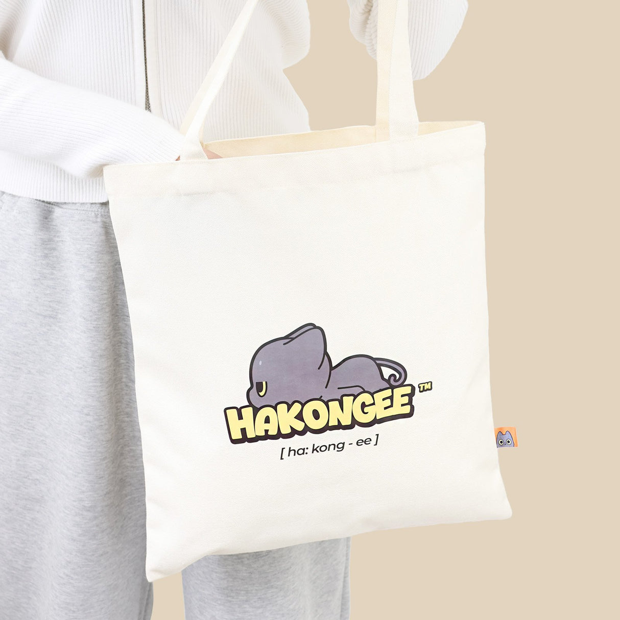 Tote bag with 'Hakongee' logo Black cat held by a person wearing a white sweater and gray pants.