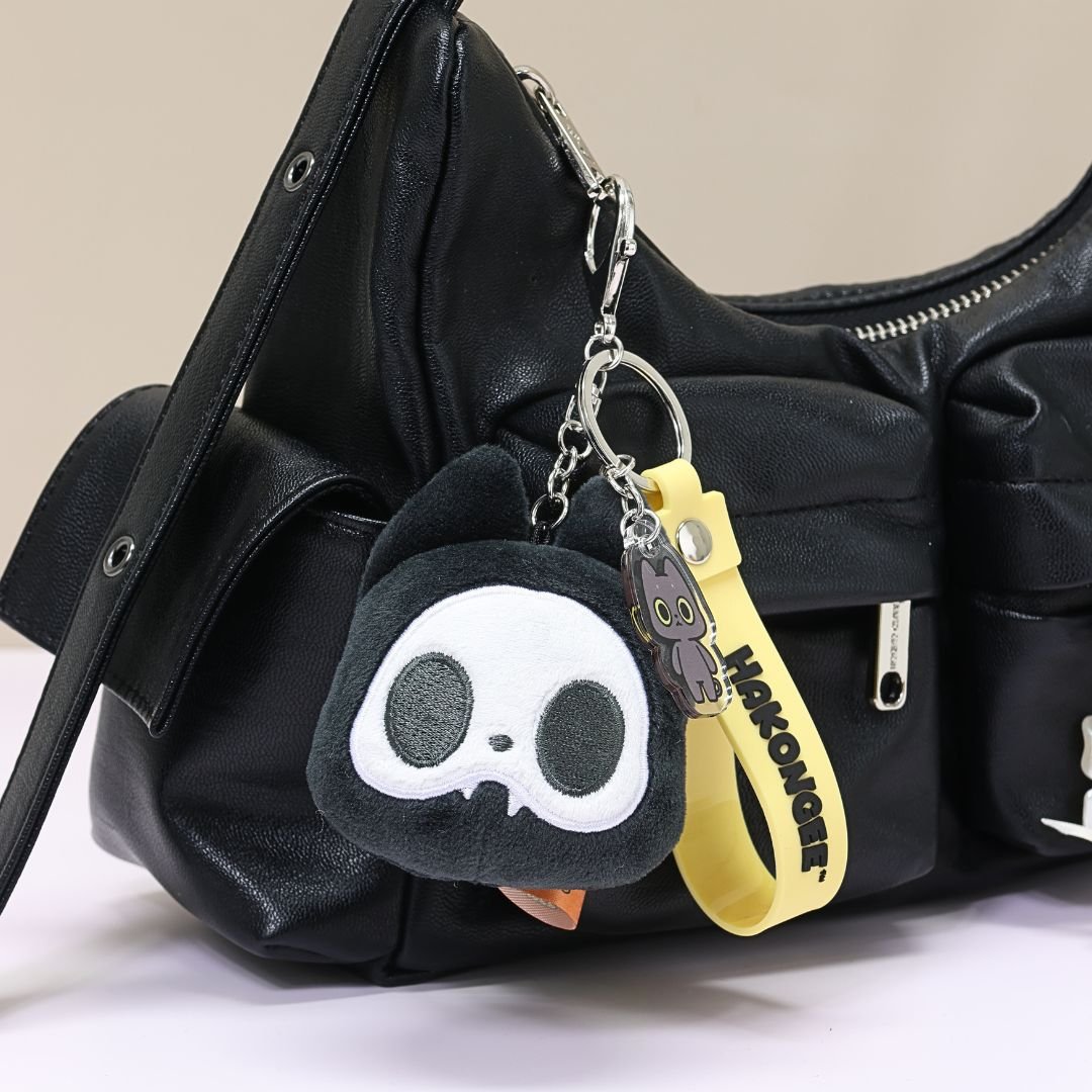 Black cat skull-shaped keychain with a yellow strap attached to a black bag.