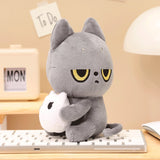 Black Cat plush cat toy holding a white Snoozy on a desk with a beige wall and 'To Do' notes in the background.