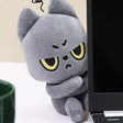 Black cat plush toy with cartoonish face next to a laptop