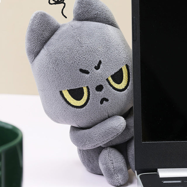 Black cat plush toy with cartoonish face next to a laptop